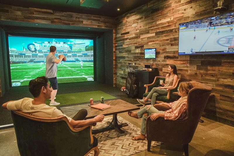 Three individuals talking and sitting with refreshments while one individual plays virtual football